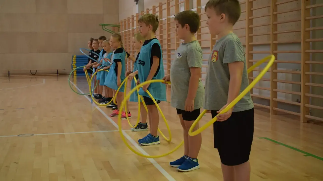 Dzieci z klas 1-3 na lekcji WF ćwiczą z hula-hop. Radosne gry i zabawy sportowe.