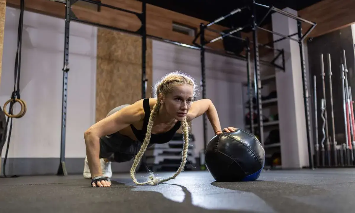 Kobieta wykonuje pompki z piłką lekarską. To przykład treningu, który pokazuje, crossfit co to jest – intensywność i wszechstronność.