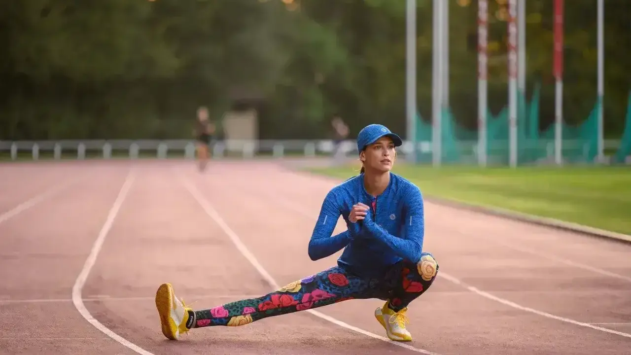 Królowa sportu w kwiecistych legginsach rozciąga się na bieżni.