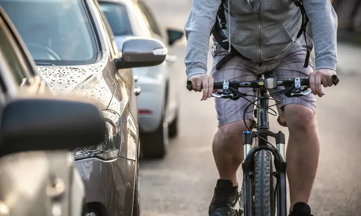 Rowerzysta jedzie obok zaparkowanych samochodów. Warto pamiętać, po jakich drogach nie można jeździć rowerem, by uniknąć niebezpiecznych sytuacji.