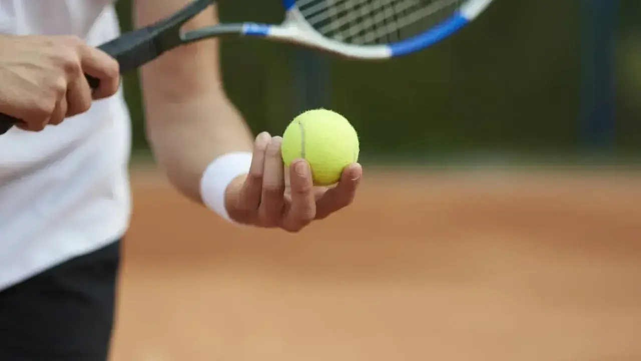Gracz trzyma piłkę tenisową, gotowy do serwisu. Kluczowy moment decydującego **tenis tie break**.