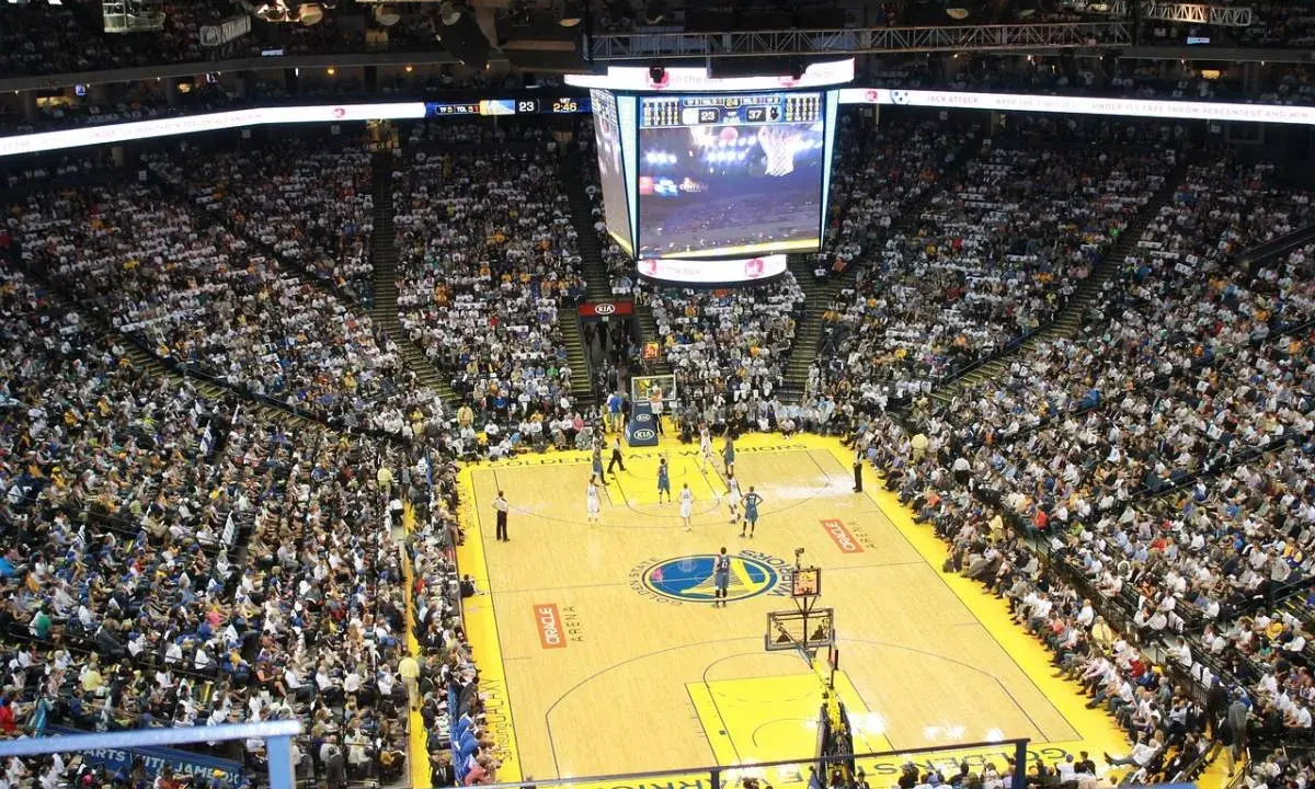 Mecz koszykówki w Oracle Arena. Na boisku gracze, na trybunach tłumy kibiców. Na telebimie widać wynik, który sugeruje, że gra jest w końcowej fazie, być może ostatni z czterech kwart.
