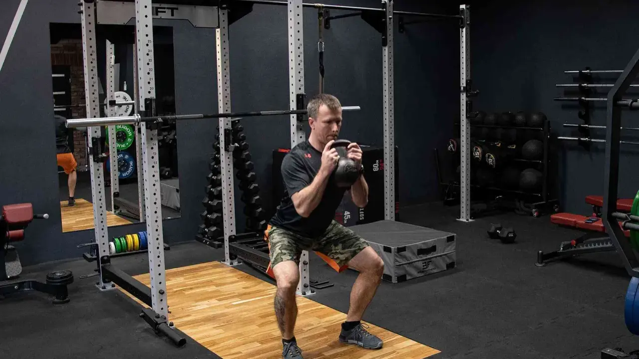 Mężczyzna wykonuje przysiad z kettlebell trzymanym w chwycie nachwyt i podchwyt.