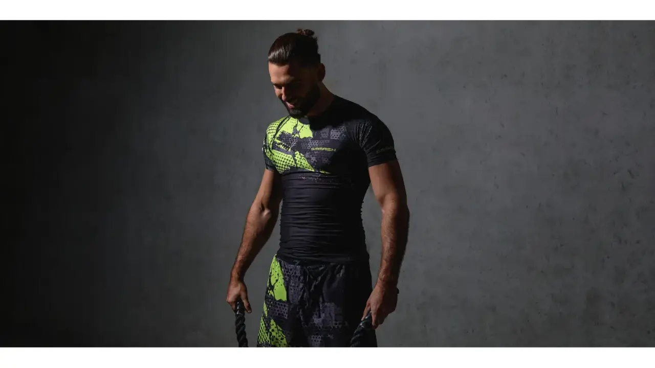 Mężczyzna w czarnym rashguardzie z neonowymi wstawkami i spodenkami, trzymający liny treningowe. Rashguard co to? Odzież sportowa.