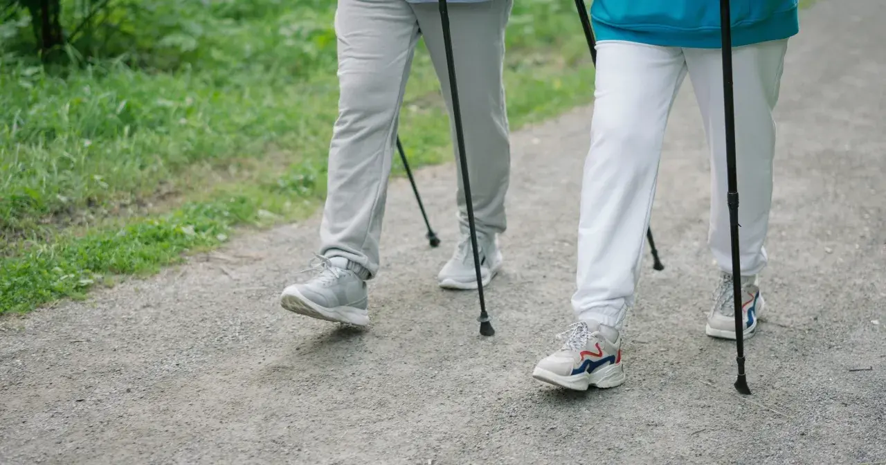Dwie osoby idące z kijkami po leśnej ścieżce. Pokazują, jak chodzić z kijkami, czerpiąc radość z aktywności na świeżym powietrzu.