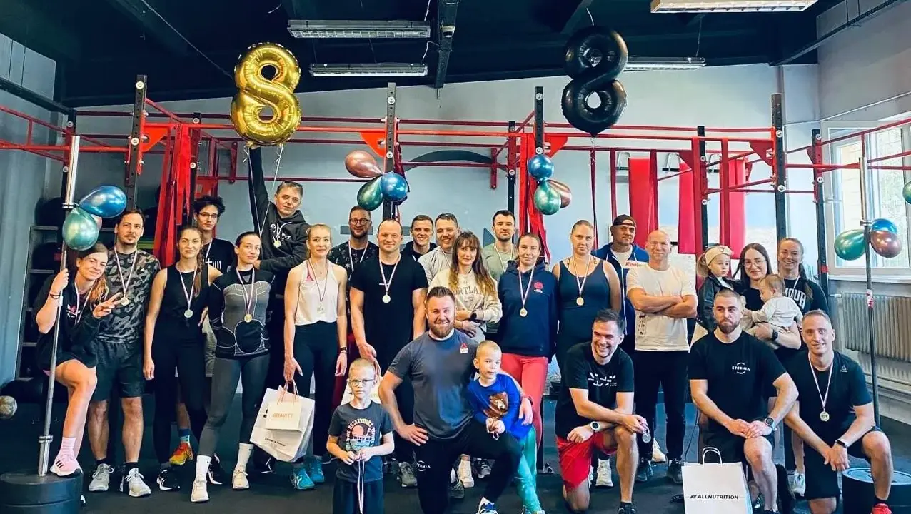 Uśmiechnięta grupa świętuje sukcesy na siłowni. Sportowe grupowe zdjęcie z medalami i balonami w kształcie ósemek.