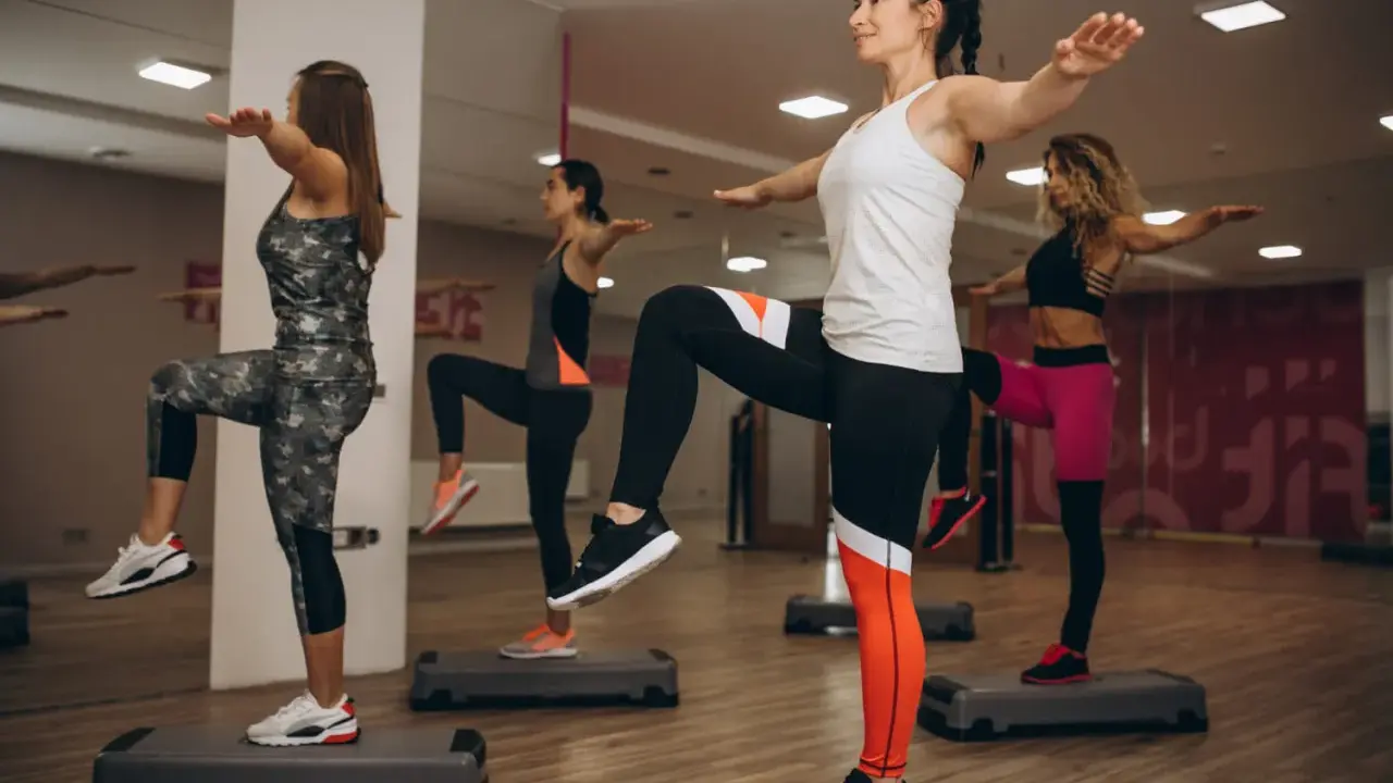 Kobiety wykonują ćwiczenia aerobowe na stepach w sali gimnastycznej.