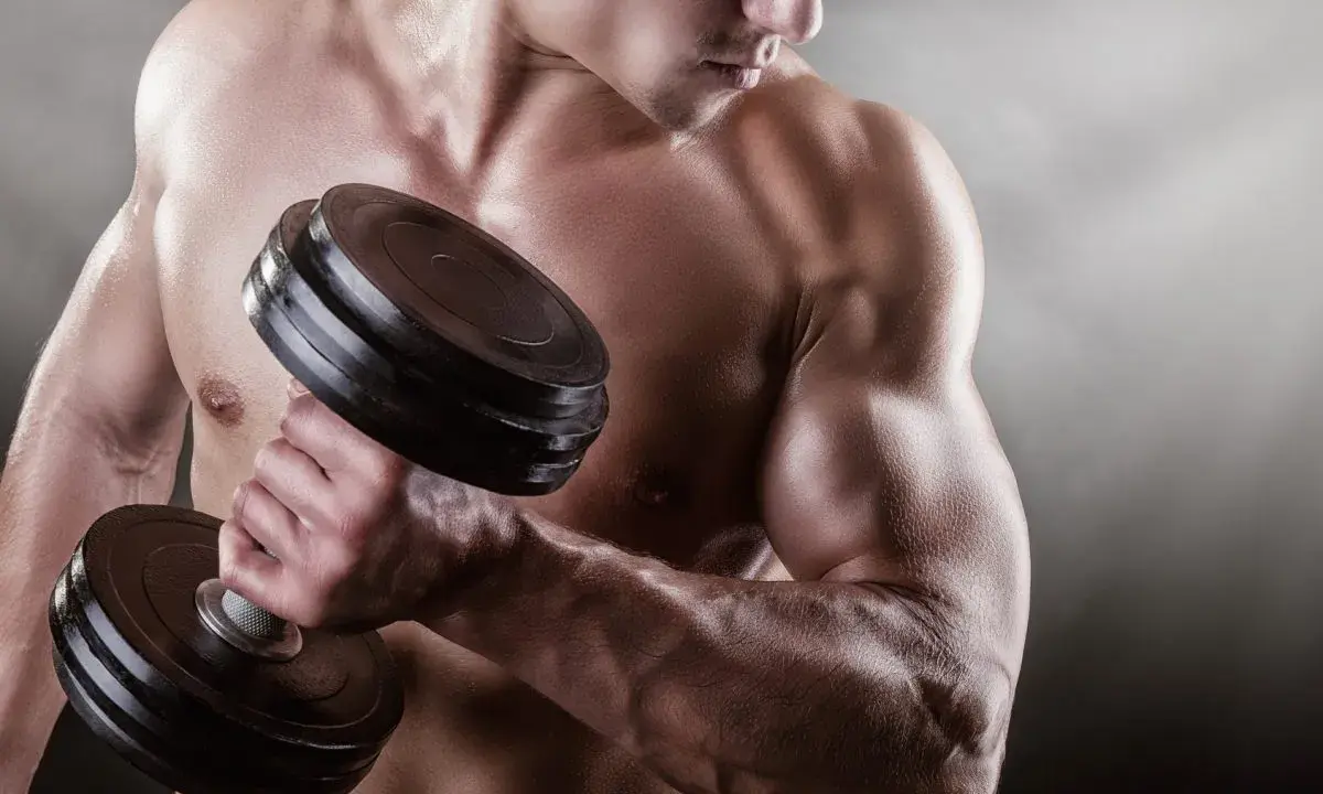 Mężczyzna podnosi ciężarek, jego napięty biceps jest wyraźnie widoczny.