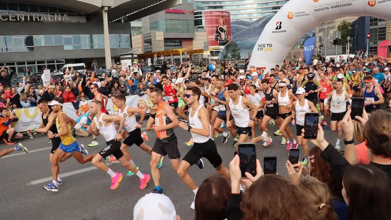 Uczestnicy maratonu w Warszawie, gotowi do startu. To świetny przykład, jak przygotować się do maratonu: trening, determinacja i wsparcie kibiców.