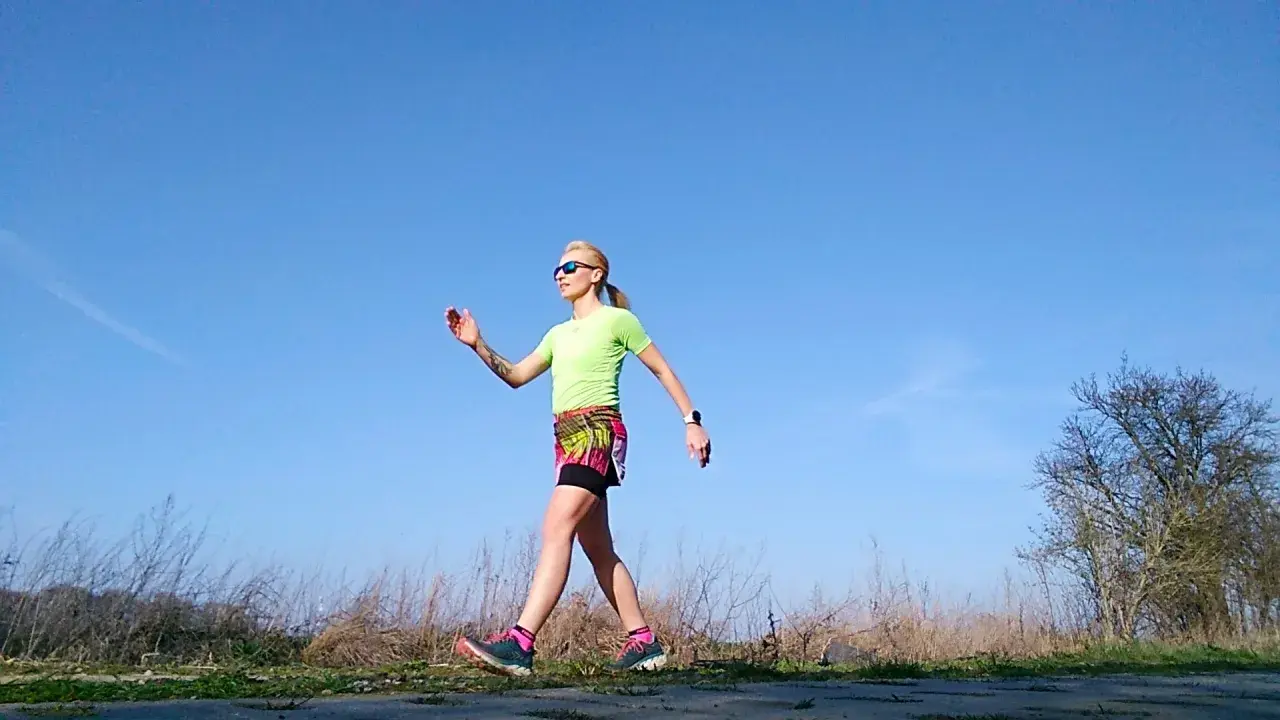 Kobieta w sportowym stroju ćwiczy marsz, stosując metodę Gallowaya. Słoneczny dzień sprzyja aktywności na świeżym powietrzu.