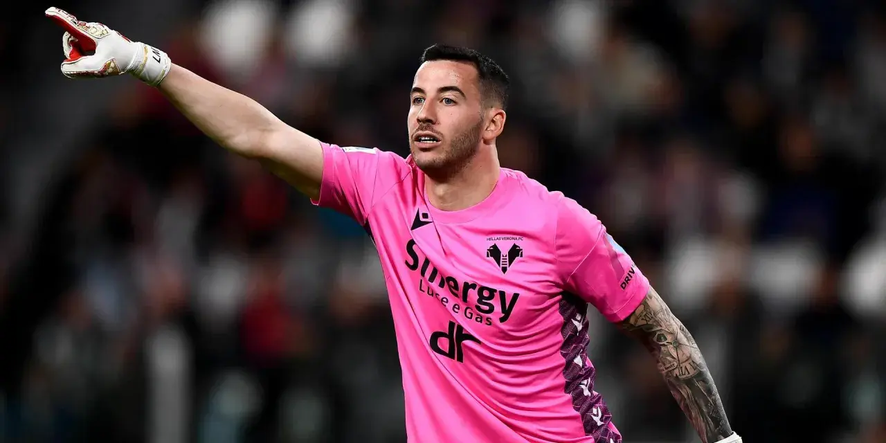 Bramkarz w różowej koszulce Hellas Verona wskazuje palcem, jakby chciał wiedzieć, ile trwa dogrywka w piłce nożnej.