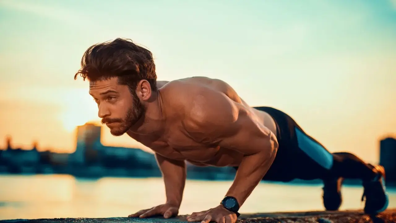 Mężczyzna wykonuje pompki na biceps przy wodzie o zachodzie słońca.