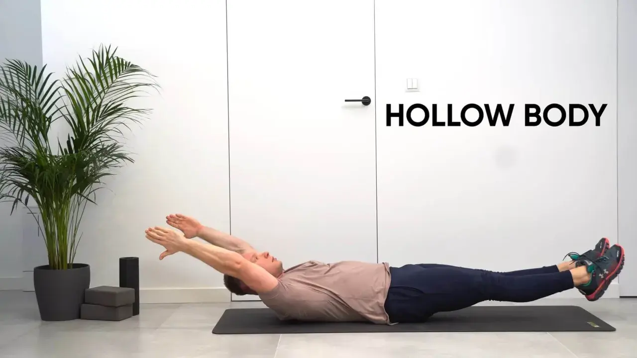 Mężczyzna ćwiczy pozycję hollow body na macie. Ręce wyciągnięte nad głowę, nogi uniesione.