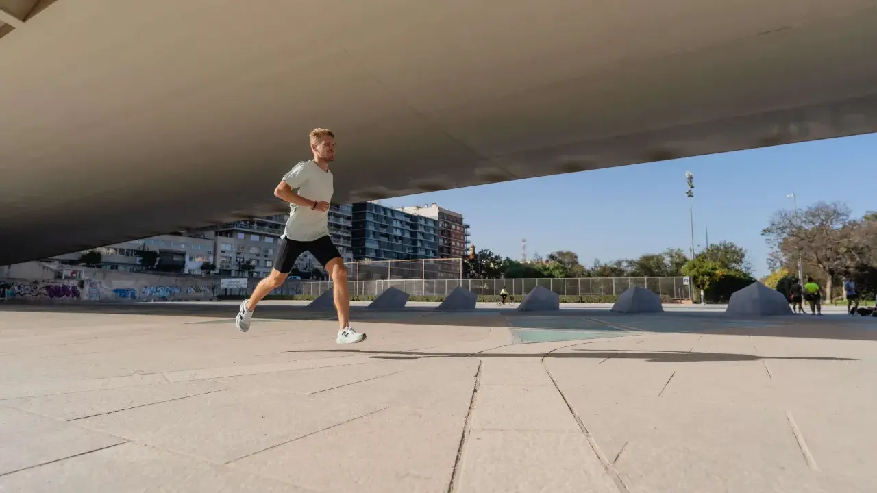 Mężczyzna w lekkim stroju sportowym biegnie po betonowym placu, przygotowując się do biegu na 10 km. W tle budynki i drzewa.