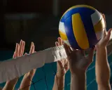 Piłka do siatkówki tuż nad siatką, ręce graczy próbują ją odbić. Czas gry zależy od wielu czynników, ale emocje są zawsze wysokie!