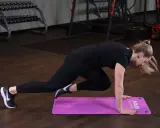 Kobieta wykonuje ćwiczenie mountain climber na fioletowej macie w siłowni.
