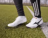 Dwa rodzaje butów piłkarskich na orliku: białe Puma z złotymi detalami i białe Mizuno Morelia.