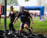 Zawodnicy pokonują tor przeszkód z opon. Kobieta i mężczyzna biegną, a za nimi inni uczestnicy. To prawdziwa survival race!