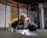 Kobieta wykonuje pompki z piłką lekarską. To przykład treningu, który pokazuje, crossfit co to jest – intensywność i wszechstronność.