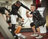 Trening EMS: Instruktor koryguje pozycję mężczyzny w kamizelce stymulującej mięśnie podczas przysiadu.
