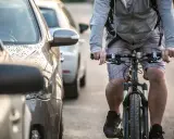 Rowerzysta jedzie obok zaparkowanych samochodów. Warto pamiętać, po jakich drogach nie można jeździć rowerem, by uniknąć niebezpiecznych sytuacji.