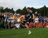 Młody mężczyzna demonstruje żonglerkę piłką na tle tłumu dzieci i dorosłych.