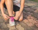 Kobieta w sportowym stroju klęczy i zawiązuje sznurówki w butach do **slow joggingu**.