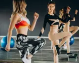 Dwie kobiety ćwiczą na stepach. Jedna w kolorowym topie i wzorzystych legginsach, druga w czarnym body i beżowych legginsach. TBC co to znaczy?