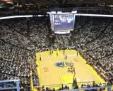 Mecz koszykówki w Oracle Arena. Na boisku gracze, na trybunach tłumy kibiców. Na telebimie widać wynik, który sugeruje, że gra jest w końcowej fazie, być może ostatni z czterech kwart.