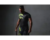 Mężczyzna w czarnym rashguardzie z neonowymi wstawkami i spodenkami, trzymający liny treningowe. Rashguard co to? Odzież sportowa.