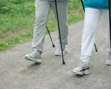 Dwie osoby idące z kijkami po leśnej ścieżce. Pokazują, jak chodzić z kijkami, czerpiąc radość z aktywności na świeżym powietrzu.
