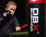 Chłopiec w rękawicach bokserskich ćwiczy ciosy przy worku treningowym. To świetny sposób na rozpoczęcie przygody z mma dla dzieci.