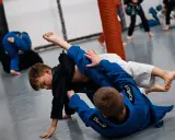 Dzieci ćwiczą jujitsu, walcząc na macie w niebieskich i czarnych kimonach.