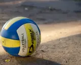 Piłka do siatkówki plażowej, niebiesko-żółta, leży na piasku. Różni się od halowej miękkością i wagą.
