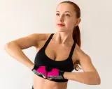 Kobieta w sportowym topie i rękawiczkach wykonuje ćwiczenia na biust, napinając mięśnie klatki piersiowej.