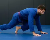 Mężczyzna w niebieskim kimonie z fioletowym pasem wykonuje ćwiczenie przygotowujące do treningu BJJ.