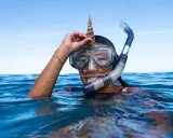 Dziewczyna w masce i fajce do snorkelingu trzyma muszlę na głowie. To właśnie snorkeling!