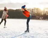 Dwie dziewczyny cieszą się jazdą na łyżwach na zamarzniętym jeziorze. Jedna z nich śmieje się radośnie, wykonując piruet.