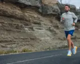 Mężczyzna w sportowym stroju biegnie po asfaltowej drodze przy skalistym zboczu. Idealny widok, by zacząć biegać i poczuć wolność.