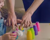 Dzieci ćwiczą z kolorowymi kubeczkami i klepsydrą. Rozwijają koordynację i spostrzegawczość.