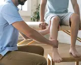 Fizjoterapeuta pomaga w domowej rehabilitacji stawu skokowego, delikatnie masując nogę pacjenta.