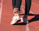 Ból kostki po bieganiu na bieżni. Sportowiec trzyma się za bolącą kostkę, czując dyskomfort.