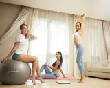 Trzy kobiety ćwiczą w domu. Jedna siedzi na piłce, druga rozciąga się, trzecia leży na macie. To świetny mel b trening pośladków!