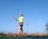 Kobieta w sportowym stroju ćwiczy marsz, stosując metodę Gallowaya. Słoneczny dzień sprzyja aktywności na świeżym powietrzu.