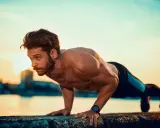 Mężczyzna wykonuje pompki na biceps przy wodzie o zachodzie słońca.