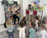Wesołe zajęcia rytmiczne w przedszkolu. Nauczycielka tańczy z dziećmi wśród zabawek na półkach.