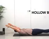 Mężczyzna ćwiczy pozycję hollow body na macie. Ręce wyciągnięte nad głowę, nogi uniesione.