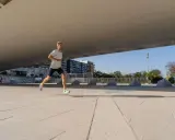 Mężczyzna w lekkim stroju sportowym biegnie po betonowym placu, przygotowując się do biegu na 10 km. W tle budynki i drzewa.