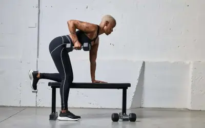 Kobieta wykonuje ćwiczenia na triceps z hantlem, opierając kolano i dłoń na ławce.