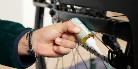Osoba aplikuje smar na łańcuch rowerowy, dbając o jego płynne działanie. Czyszczenie łańcucha rowerowego to klucz do sprawnej jazdy.